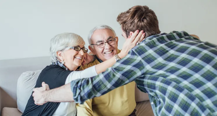 Young man embracing his smiling elderly parents on a couch – Representing family financial planning, retirement security, and generational wealth management.